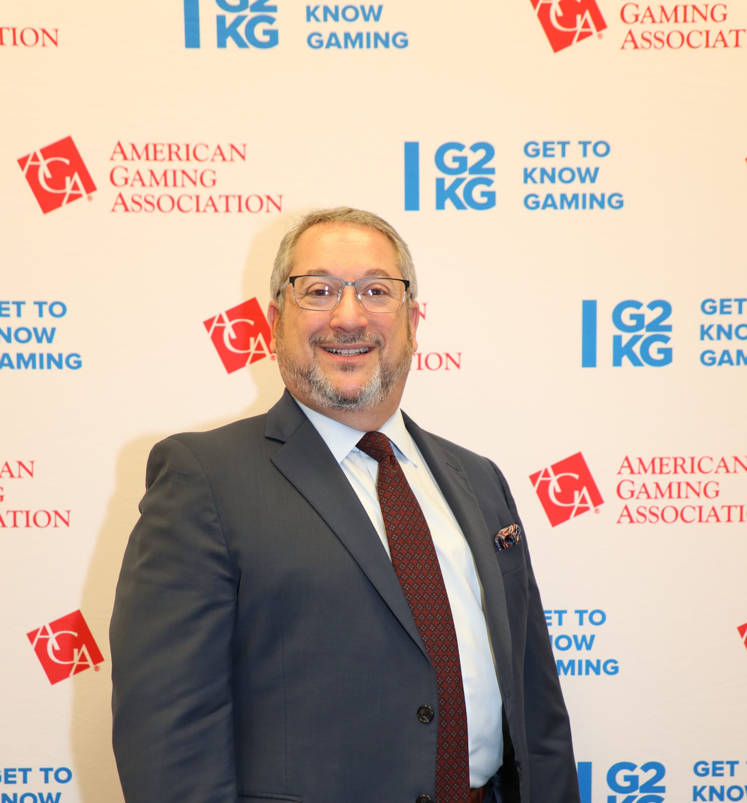 A man in a suit and tie smiles while standing in front of a backdrop featuring logos for the American Gaming Association and "Get to Know Gaming.