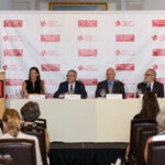 A panel of six speakers, including one standing at a podium, addresses an audience during a Responsible Gaming event. The backdrop displays logos of the American Gaming Association and Responsible Gaming.