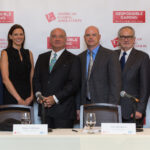 Six people in formal attire stand together in front of a backdrop with "American Gaming Association" and "Responsible Gaming" logos. A table with nameplates and microphones is in front of them.