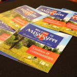 Brochures on a table with "Welcome to Mississippi: Birthplace of America's Music" written on the cover. The brochures also have a section titled "Casinos & Communities," displayed against an outdoor scenic background.