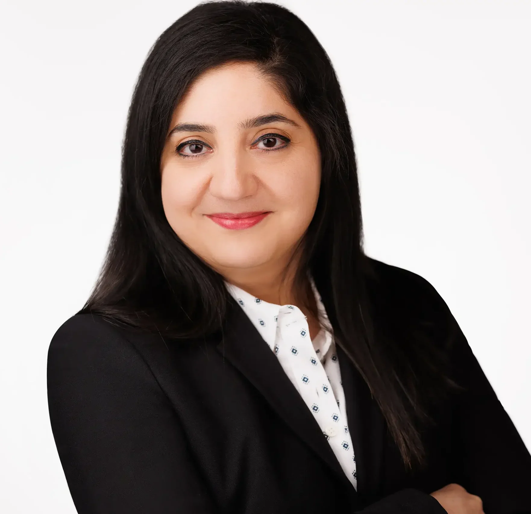 A person with long, dark hair is smiling, wearing a black blazer over a white shirt with a subtle pattern. The individual is posing against a plain, light background.