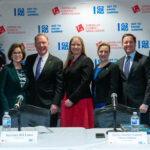 A group of seven people, four men and three women, stand together smiling in front of a backdrop with logos for the American Gaming Association and "Get to Know Gaming." Two name placards label individuals as Secretary Bill Lance and Deputy Attorney General Chrissi Nimmo.