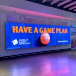 A large digital sign in an indoor space displays the message "Have a Game Plan" in bold letters. Below it are the logos of the American Gaming Association and a basketball with "Keep It Social" written on it.