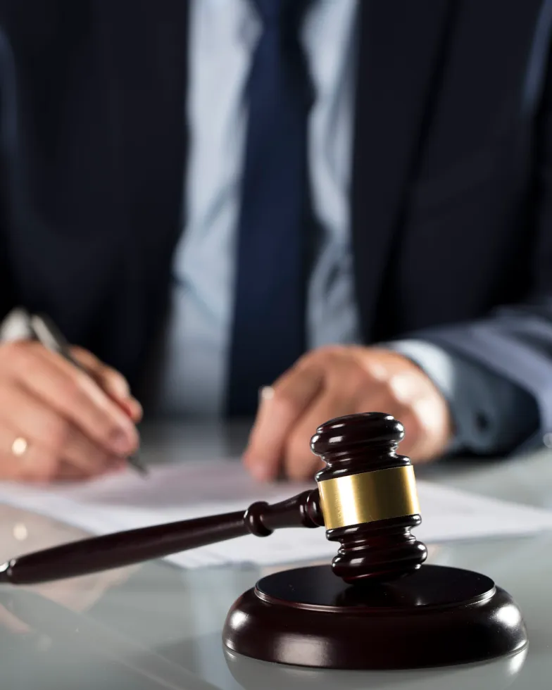 A person in a suit writes on papers at a desk, with a judge’s gavel in focus in the foreground, symbolizing law or legal proceedings related to illegal gambling.
