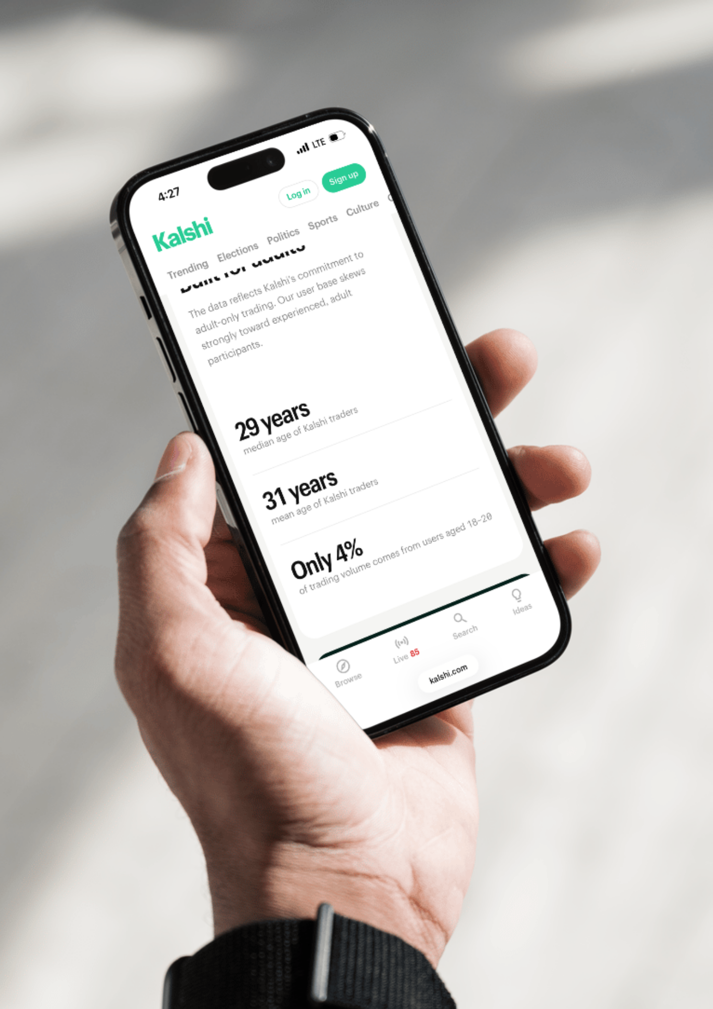 A hand holds a smartphone displaying a Kalshi website page with statistics about market traders, showing ages 29 years and 31 years, and “Only 4%” in bold. The screen is viewed in bright natural light.
